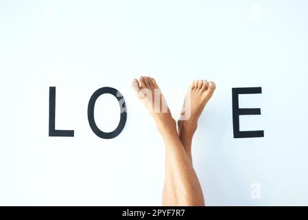 Ich werde gehen, bis ich eines Tages Liebe finde. Studiofoto eines unbekannten mannes kreuzte die Beine mit den Füßen und formte den Buchstaben V im Wort LIEBE. Stockfoto