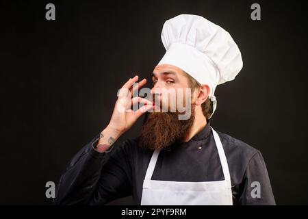 Der Mann des Küchenchefs in Uniform und die weiße Schürze zeigen das Schild in Ordnung. Bärtiger Koch mit Köchmütze mit Geste für den Restaurantservice. Professionelle Kochshows Stockfoto