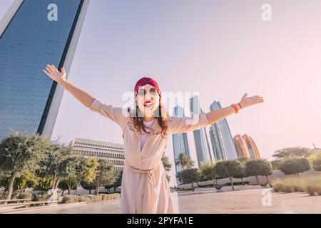 Lassen Sie Ihre Sinne von der Gegenüberstellung des fließenden Kleides einer indischen Frau und den eleganten Linien der majestätischen Wolkenkratzer von Abu Dhabi verzaubern. Stockfoto