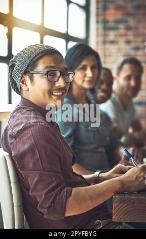 Ich kann nicht, aber wir können es. Ein junger Mann mit einem Team von Unternehmern, die in einem modernen Büro zusammenarbeiten. Stockfoto