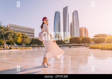 Erleben Sie die Verschmelzung von Moderne und Tradition, während eine indische Frau vor dem Hintergrund von Abu Dhabis berühmten Wolkenkratzern spaziert. Stockfoto