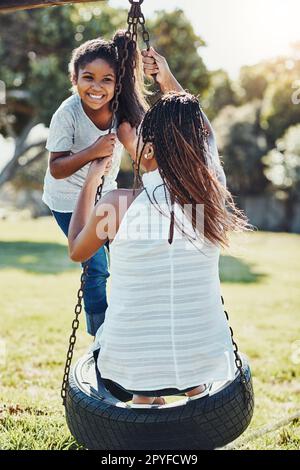 Das wird ein Tag voller Spaß. Eine Mutter schubst ihre Tochter auf eine Schaukel im Park. Stockfoto