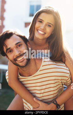 Das ist bei weitem meine Liebesgeschichte. Portrait eines glücklichen jungen Mannes, der seine Freundin mit dem Huckepack draußen mitnimmt. Stockfoto
