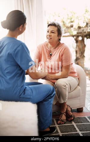 Ich weiß nicht, was ich ohne Ihre Unterstützung tun würde. Eine junge Krankenschwester, die eine ältere Frau behaglich an den Händen hält. Stockfoto