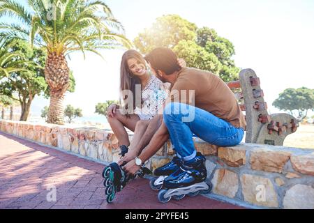 Bereit zum Abrollen. Eine Frau, die ihrem Freund hilft, Rollerblades in einem Park anzuziehen. Stockfoto