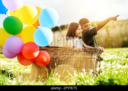 Sehen wir uns an, was hinter dieser Wolke steckt. Ein Paar niedliche Geschwister, die mit einem Korb spielen und ein paar Ballons draußen. Stockfoto