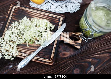 Zerkleinern von Zitrone und schwarzer Holunderbeere auf einem Schneidebrett zur Herstellung eines Kräutergetränks oder eines Medikaments zur Heilung von Sirup aus Holunderblüten zu Hause. Stockfoto