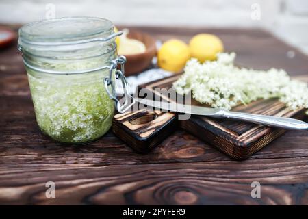 Zerkleinern von Zitrone und schwarzer Holunderbeere auf einem Schneidebrett zur Herstellung eines Kräutergetränks oder eines Medikaments zur Heilung von Sirup aus Holunderblüten zu Hause. Stockfoto