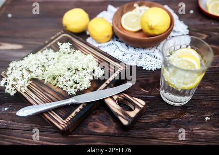 Zerkleinern von Zitrone und schwarzer Holunderbeere auf einem Schneidebrett zur Herstellung eines Kräutergetränks oder eines Medikaments zur Heilung von Sirup aus Holunderblüten zu Hause. Stockfoto