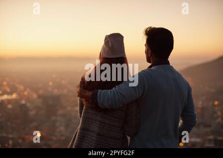 Es gibt niemanden, mit dem ich diese Ansicht lieber teilen möchte. Rückblick auf ein liebevolles junges Paar, das bei Tagesanbruch die Aussicht auf die Stadt bewundert. Stockfoto