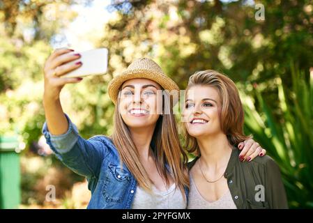 Kommen Sie noch mal rein. Zwei attraktive junge Frauen, die draußen Selfies machen. Stockfoto