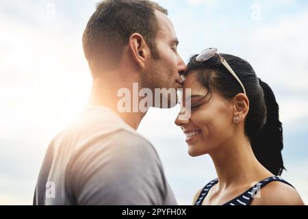 Wahre Liebe ist ein Kuss auf die Stirn. Ein junger Mann küsst seine Freundin liebevoll draußen auf die Stirn. Stockfoto