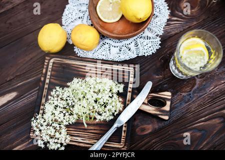 Zerkleinern von Zitrone und schwarzer Holunderbeere auf einem Schneidebrett zur Herstellung eines Kräutergetränks oder eines Medikaments zur Heilung von Sirup aus Holunderblüten zu Hause. Stockfoto