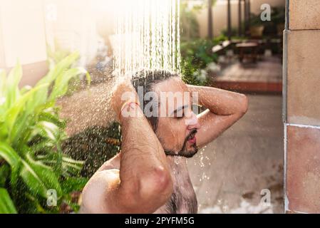 Ein Mann, der eine Außendusche in einem Traumurlaub-Resort nimmt. Stockfoto