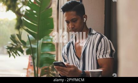 Der junge Mann sitzt draußen und benutzt ein Handy Stockfoto