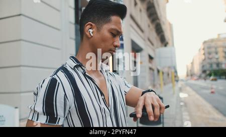 Ein junger Mann, der Musik hört, auf seine Armbanduhr schaut Stockfoto