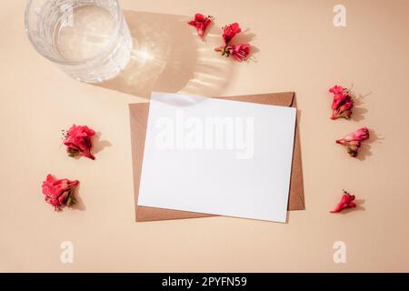 Umschlag mit unbeschrifteter Karte, roten Rosskastanienblumen und Glas Wasser mit rauem, neutralem beigefarbenem Hintergrund. Grußkarte. Draufsicht, flach l Stockfoto
