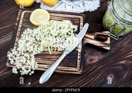 Zerkleinern von Zitrone und schwarzer Holunderbeere auf einem Schneidebrett zur Herstellung eines Kräutergetränks oder eines Medikaments zur Heilung von Sirup aus Holunderblüten zu Hause. Stockfoto