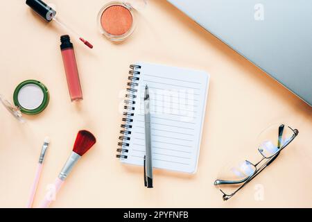 Unbeschrifteter Notizblock mit Stift, Brille, Notizbuch und Make-up-Kosmetik auf neutralem beigefarbenem Hintergrund. Beauty-Blogger-Konzept. Draufsicht, flach liegend. Stockfoto