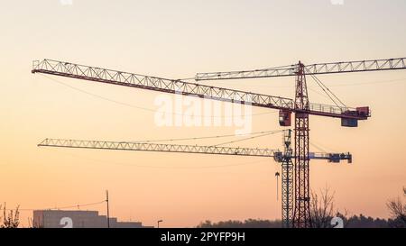 Baustelle am Abendhimmel. Baustelle mit drei Hebevorrichtungen, Kräne auf rotem Himmelshintergrund Stockfoto