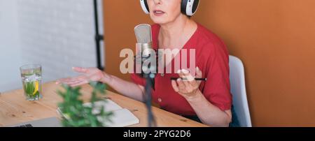 Banner Nahaufnahme Frau, die Podcasts für ihre Online-Show aufnimmt. Attraktive Geschäftsfrau, die Kopfhörer auf der Vorderseite des Mikrofons für eine Radiosendung verwendet Stockfoto