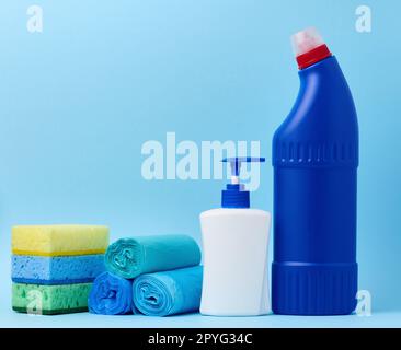 Weiße Kunststoffflasche mit Spender und Müllsäcken, Schwämme und blaue Flasche mit Reinigungsmittel auf blauem Hintergrund Stockfoto