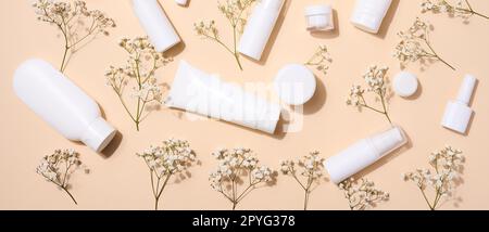 Weiße Kunststoffröhrchen, Gefäße und Zweige von Gypsophila auf beigefarbenem Hintergrund, Behälter für kosmetische Cremes und Gele, Werbung und Markenwerbung, Draufsicht Stockfoto