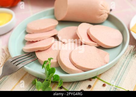 Zusammensetzung mit gekochter Wurst auf dem Teller, grünen Zwiebeln und Sauce auf einem rosa Fliesentisch Stockfoto