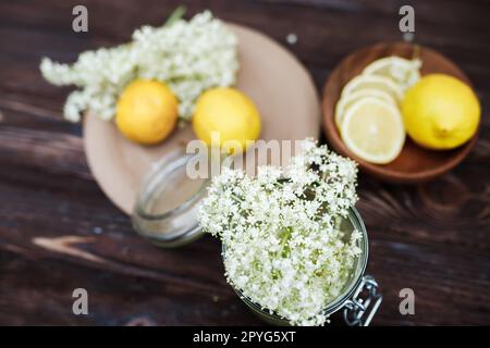 Draufsicht der Zutaten für ein erfrischendes Sommergetränk aus Holunderbeersirup und Zitronen. Frisch geschnittene Holunderblumen und geschnittene Zitronen auf einem Stockfoto