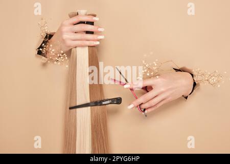 Hände mit Blumen halten Haarsträhnen für Verlängerungen auf beigefarbenem Hintergrund. Stockfoto