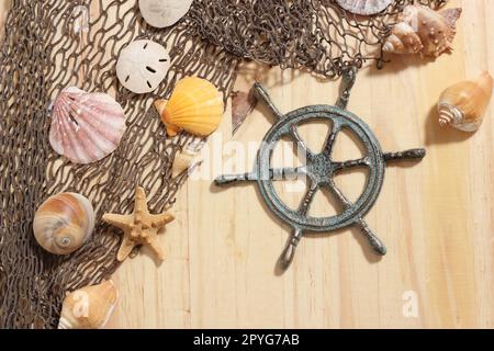 Captains Wheel mit Fischernetz und Meeresmuscheln auf Holzhintergrund Stockfoto