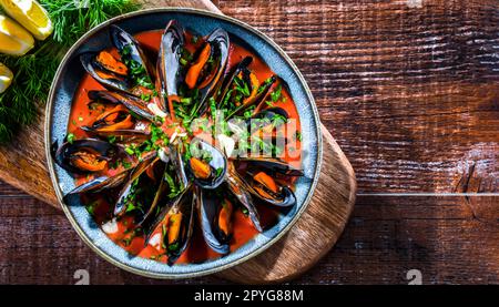 Ein Teller mit Muscheln in Tomatensoße, serviert mit Petersilie und Zitrone Stockfoto