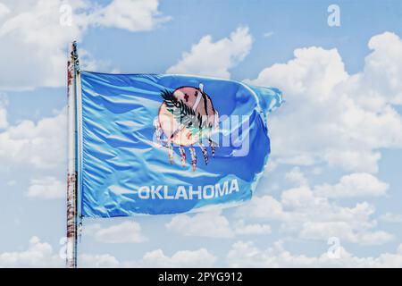 Die Flagge von Oklahoma, die im wolkigen Himmel über dem rostigen Fahnenmast im US-Bundesstaat winkt Stockfoto