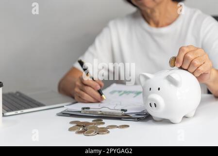Eine Frau, die Geld in Sparschwein steckt und Geld für zukünftige Pläne und Pensionsfonds spart. Stockfoto