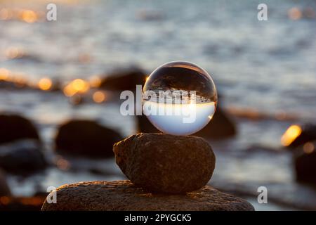 Die Glaskugel liegt auf dem obersten Stein, der den Strand und das Meer reflektiert Stockfoto