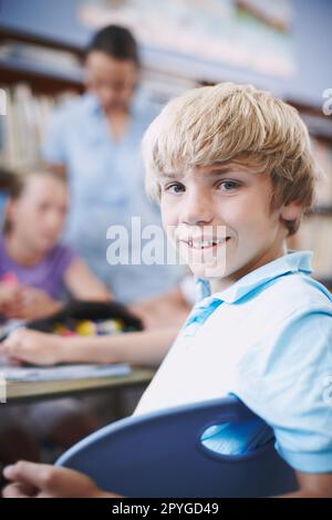 Ich genieße die Schule wirklich. Ein aufgeregter Junge, der mit seinen Klassenkameraden in der Bibliothek sitzt. Stockfoto