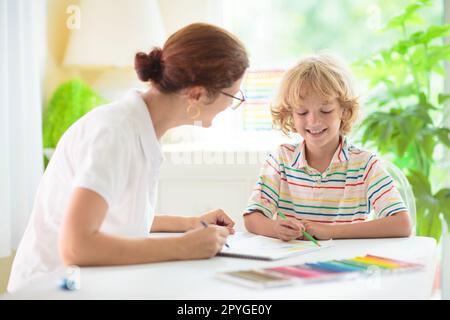 Kindzeichnung. Ein Schulkind malt ein Bild. Ein kleiner Junge mit bunten Bleistiften macht Hausaufgaben in einem weißen, sonnigen Raum. Kinder zeichnen und malen. Stockfoto