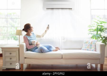 Frau mit Fernbedienung der Klimaanlage. Angenehme Temperatur zu Hause. Kühl- und Heizgerät. Klimaanlage an heißen Sommertagen. Stockfoto