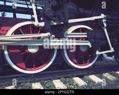 Retro-Räder einer Lokomotive oder eines Zuges aus nächster Nähe. Rote große Schwermetallräder mit Kolbenführungsmechanismen. Lokomotive des 19. - 20. Jahrhunderts mit einer Dampfmaschine. Retro-Style. Stockfoto