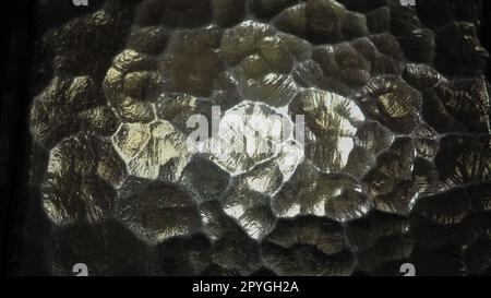 Wellglas, Rücklichtquelle. Spiel von Blendungen und Reflexionen auf einer transparenten, unebenen Oberfläche. Dunkle und helle abstrakte asymmetrische, mehrfach beleuchtete Ebenen. Abstrakter, holpriger brauner Hintergrund Stockfoto