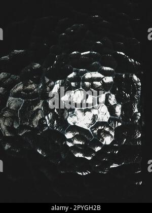 Wellglas, Rücklichtquelle. Das Spiel von Blendung und Reflexionen auf einer transparenten, unebenen Oberfläche. Dunkle und helle abstrakte asymmetrische, mehrfach beleuchtete Ebenen. Abstrakter seltsamer Hintergrund Stockfoto