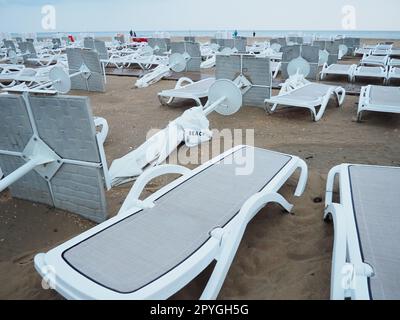 Ein Strandschirm liegt nach schlechtem Wetter auf einem Sandstrand gefaltet. Sturm auf See. Ende der Strandsaison durch Taifun und Zyklon. Liegestühle, Sonnenschirme und Hotelmöbel. Windgedrehte Strukturen Stockfoto