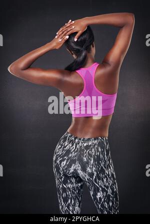 Sie dehnt sich, um die Muskeln zu stärken. Studioaufnahme im Rückspiegel einer Frau, die sich vor schwarzem Hintergrund dehnt. Stockfoto