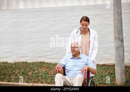 Sie macht eine Spritztour mit ihrer Patientin. Eine Ärztin schubste ihren älteren Patienten im Rollstuhl nach draußen. Stockfoto