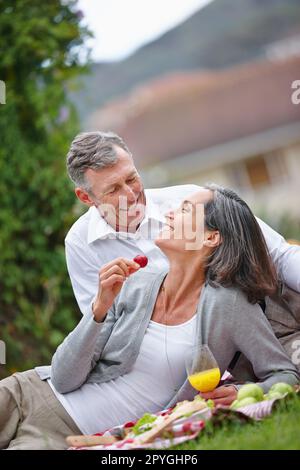 Die Romantik am Leben erhalten. Ein liebevolles, reifes Paar, das ein romantisches Picknick auf dem Rasen macht. Stockfoto