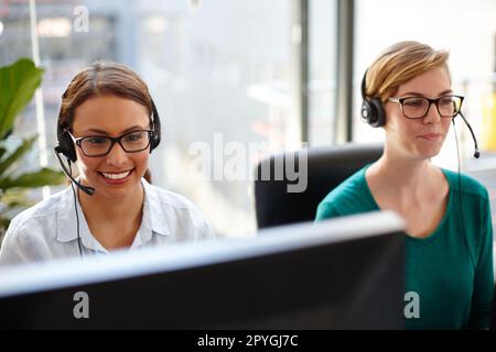 Bereitstellung von Online-Support für ihre Kunden. Zwei weibliche Kundendienstmitarbeiter nehmen Anrufe in ihrem Büro entgegen. Stockfoto