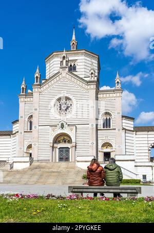 Von außen befindet sich das Famedio, die Halle des monumentalen Friedhofs von Mailand, auf dem viele bemerkenswerte Menschen begraben sind, wobei zwei Personen auf einer Bank sitzen. Stockfoto