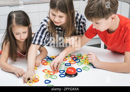 Lächelnde, nachdenkliche Kinder von Jungen und Mädchen verbinden bunte Kettenfiguren und bilden Puzzlekonstruktoren. Entwicklung von Kindern Stockfoto