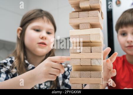 Konzentrierte und leidenschaftliche Kinder, die gemeinsam ein Brettspiel des Balancewalls aus hölzernen Ziegelsteinen spielen. Kommando-Kinderschlacht Stockfoto