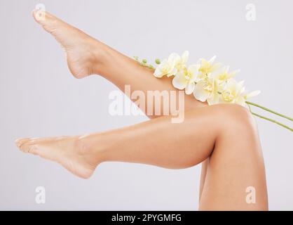 Beine, Schönheit und Hautpflege mit Blüten und natürlichem Schein mit Naturästhetik, Kosmetik und gesunder Haut vor Studiohintergrund. Füße, kosmetische Pflege und Glanz mit Pediküre, Wellness und Orchidee. Stockfoto